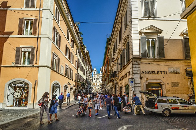 A street view shot of a busy shopping area in Rome with 4 story orange buildings on both sides of a narrow street.